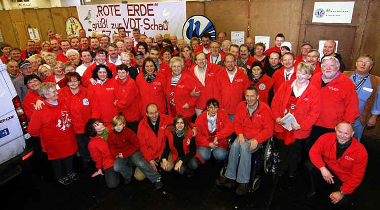 Großes Gruppenfoto der Mitglieder in roten Rote-Erde-Jacken vor dem Transparent „Rote Erde grüßt zur VDT-Schau“